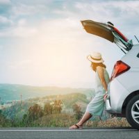 Woman traveler sitting on hatchback car with mountain background in vintage tone