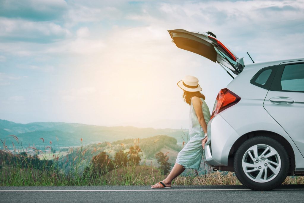 Woman traveler sitting on hatchback car with mountain background in vintage tone